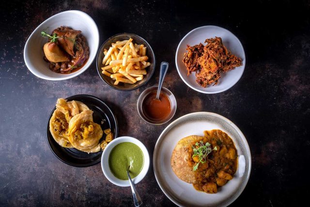 A crisp Punjabi samosa served with fresh onion bhaji and vibrant green chutney, prepared for vegetarian takeaway at Masalchi in London.