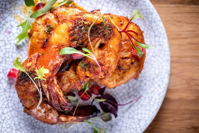 A vibrant jumbo prawn tikka coated in rich tandoori masala, served as a signature Indian street food dish at Chef Atul Kochhar's Wembley Park restaurant.