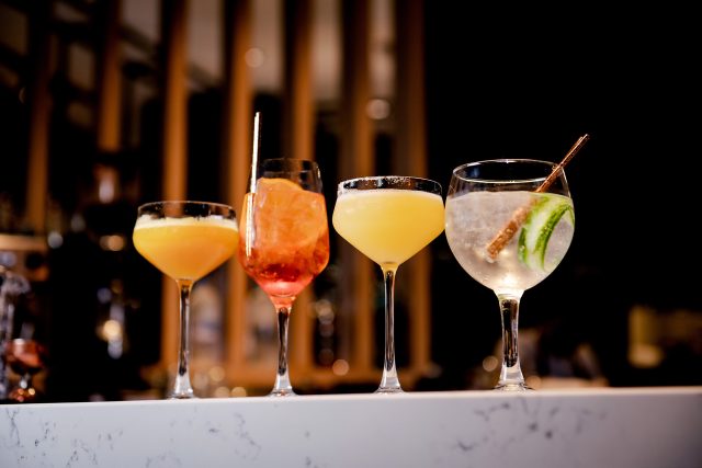 Four bespoke craft cocktails resting on a pristine marble bar, ready for a vibrant New Year's Eve celebration at Chef Atul Kochhar's Wembley Park restaurant.