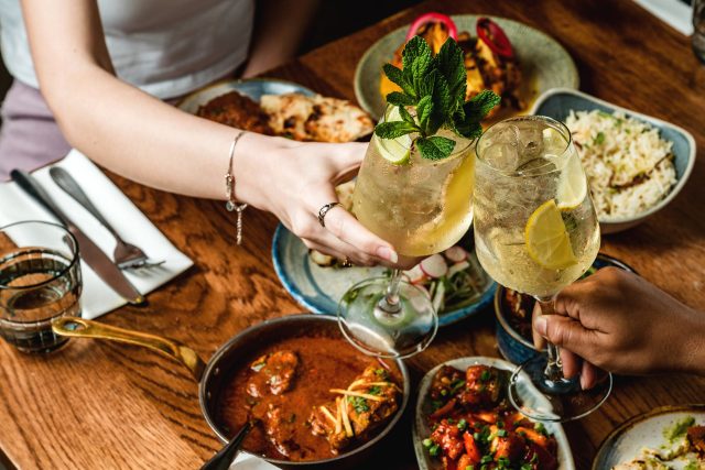 Toasting with cocktails over a table filled with Indian curries, rice, and naan at Masalchi in Wembley Park.